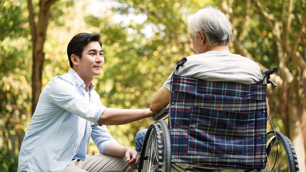 молодой человек утешает старика в инвалидном кресле