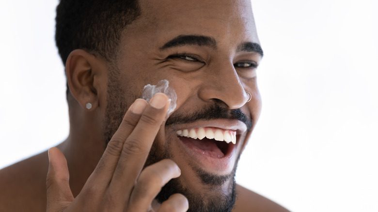чернокожий мужчина наносит крем на лицо счастливый уход за кожей