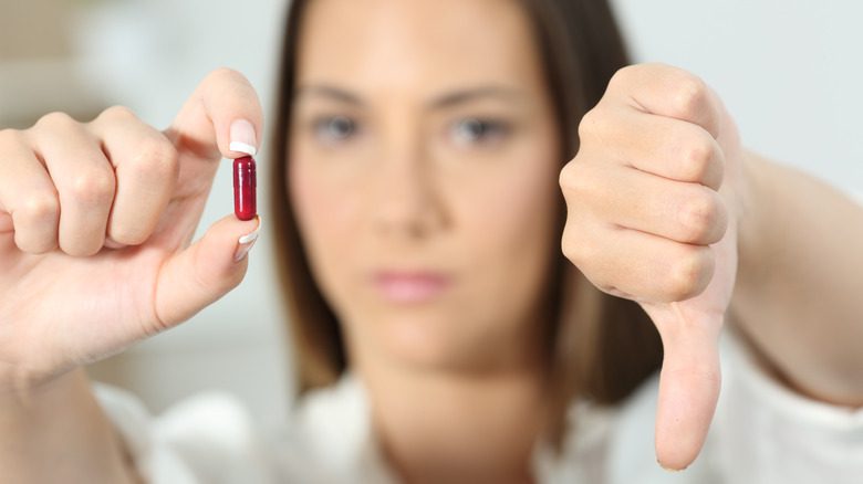 Женщина держит в одной руке красную таблетку, а другой рукой показывает большой палец вниз