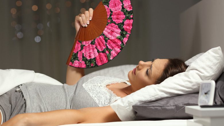 женщина обмахивает себя веером в постели