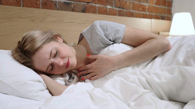 Женщина в постели держится за горло от боли
