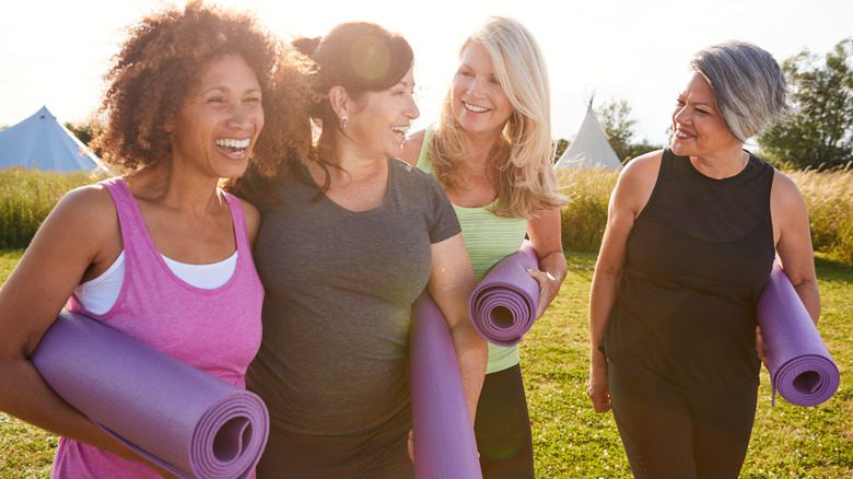 Женщины несут коврики для йоги и улыбаются