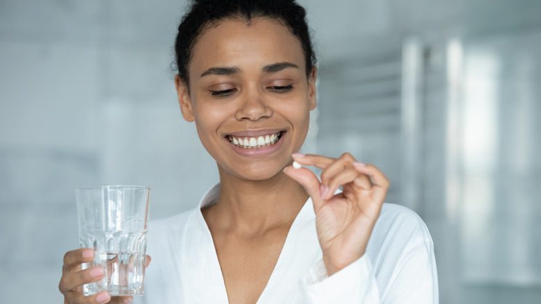 женщина держит таблетку витамина С и стакан воды