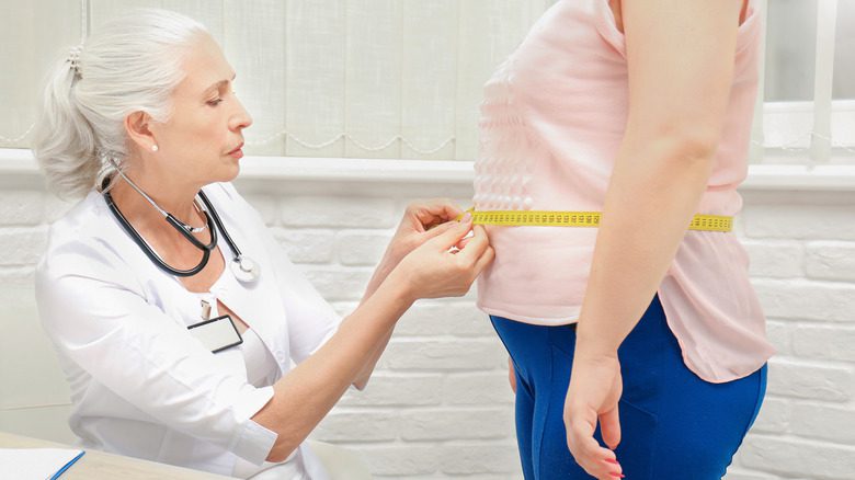 врач измеряет талию пожилой женщины