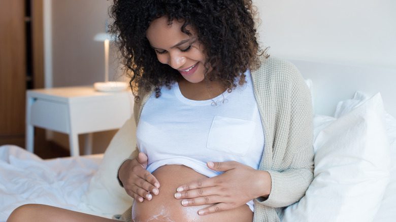 Беременная женщина наносит увлажняющий крем