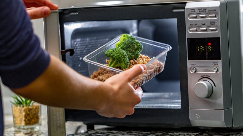мужчина разогревает еду в пластиковом контейнере в микроволновой печи