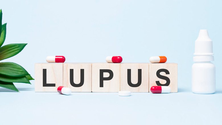 Слово LUPUS составлено из строительных кубиков. Ряд деревянных кубиков со словом, написанным черным шрифтом, расположен на белом фоне.
