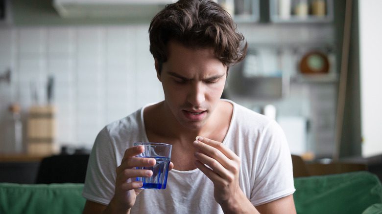 Мужчина держит стакан с водой и таблетку 