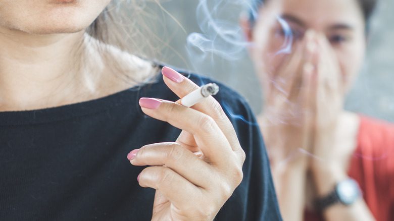 женщина держит зажженную сигарету и курит