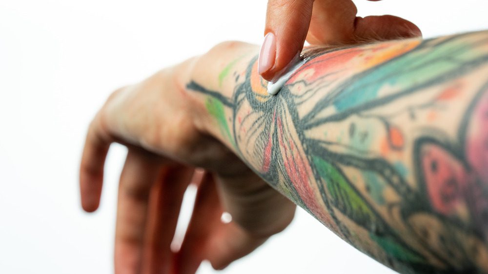 Крупный план женщины, наносящей крем на татуировку