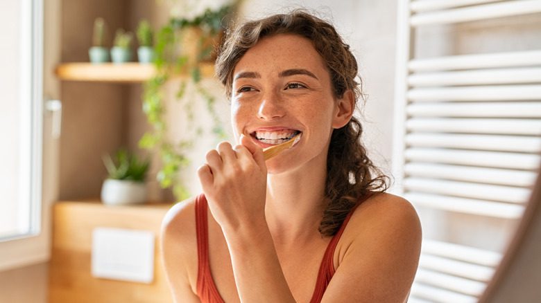 Женщина улыбается и держит зубную щетку во рту