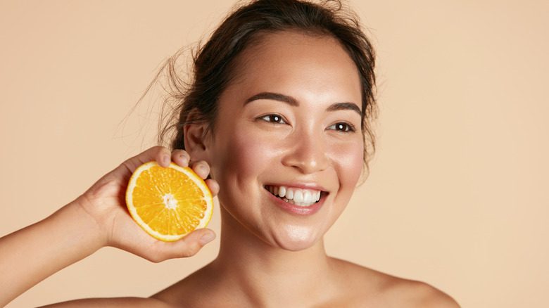 женщина с красивой кожей держит апельсин