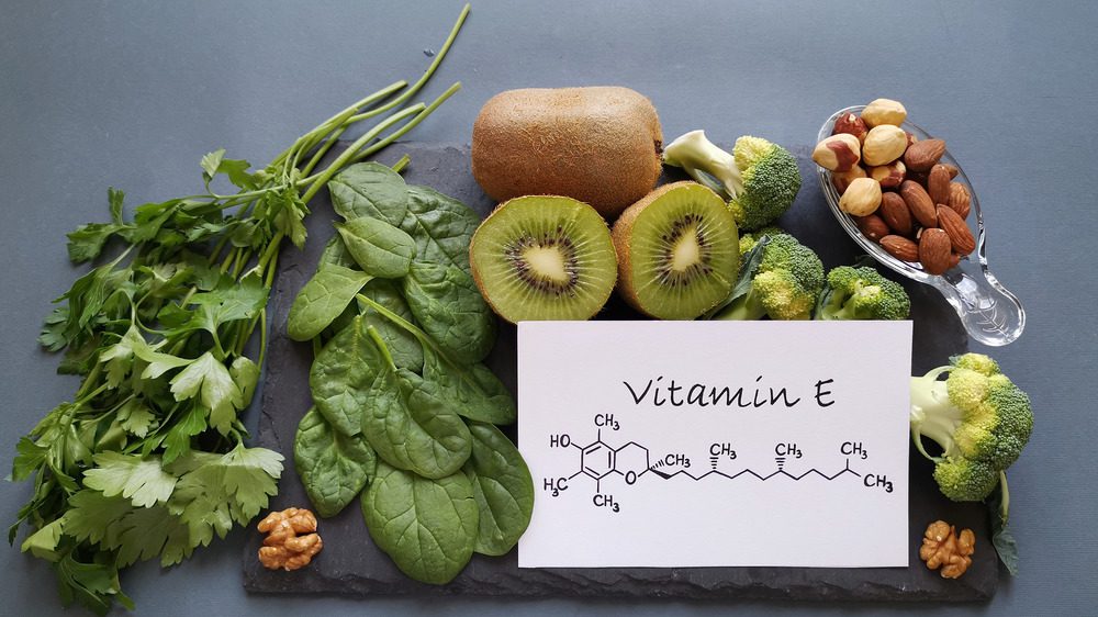 Витамин Е на бумаге в окружении листовых овощей и фруктов