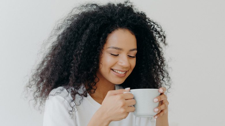 Женщина улыбается и смотрит на белую кружку с кофе