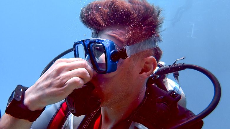 Подводный ныряльщик зажимает нос и надевает кислородную маску