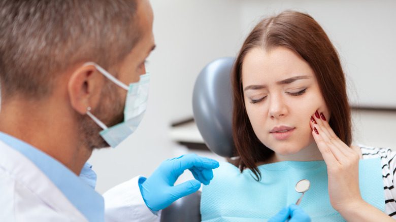 Женщина у стоматолога держится за рот от боли