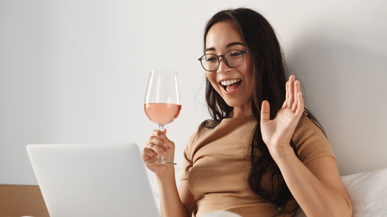 Женщина держит бокал вина, разговаривая по ноутбуку