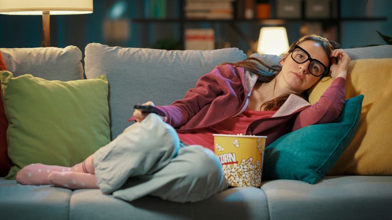 женщина на диване с попкорном и пультом от телевизора
